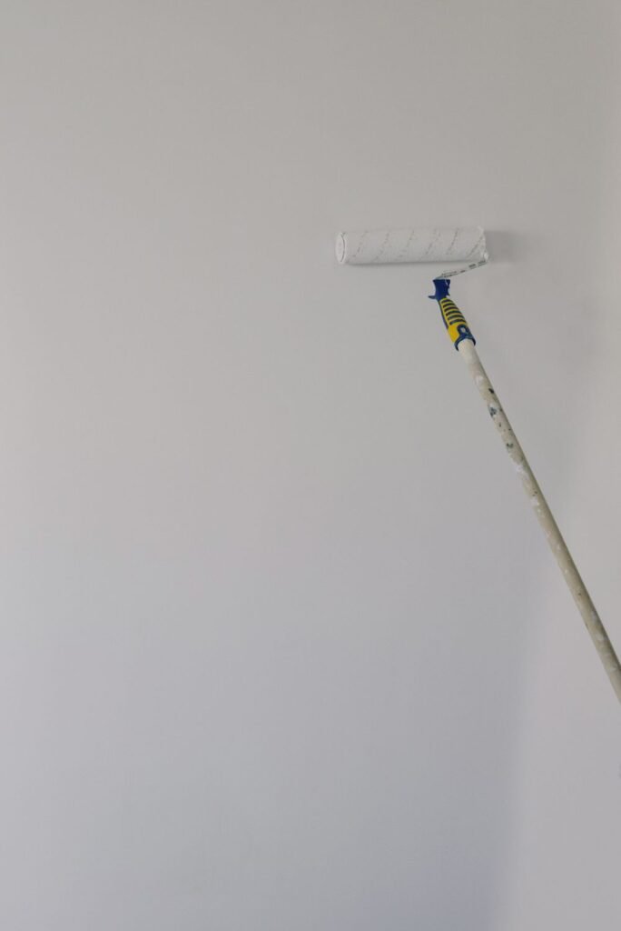 Paint roller on a long handle applying white paint to an interior wall